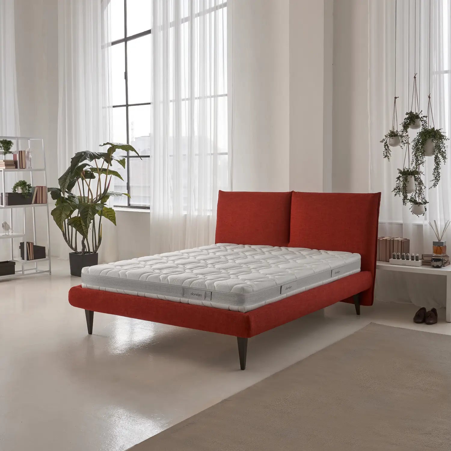 A minimalist red bed frame with the Dorelan Essential mattress in a bright room with natural lighting and plants.