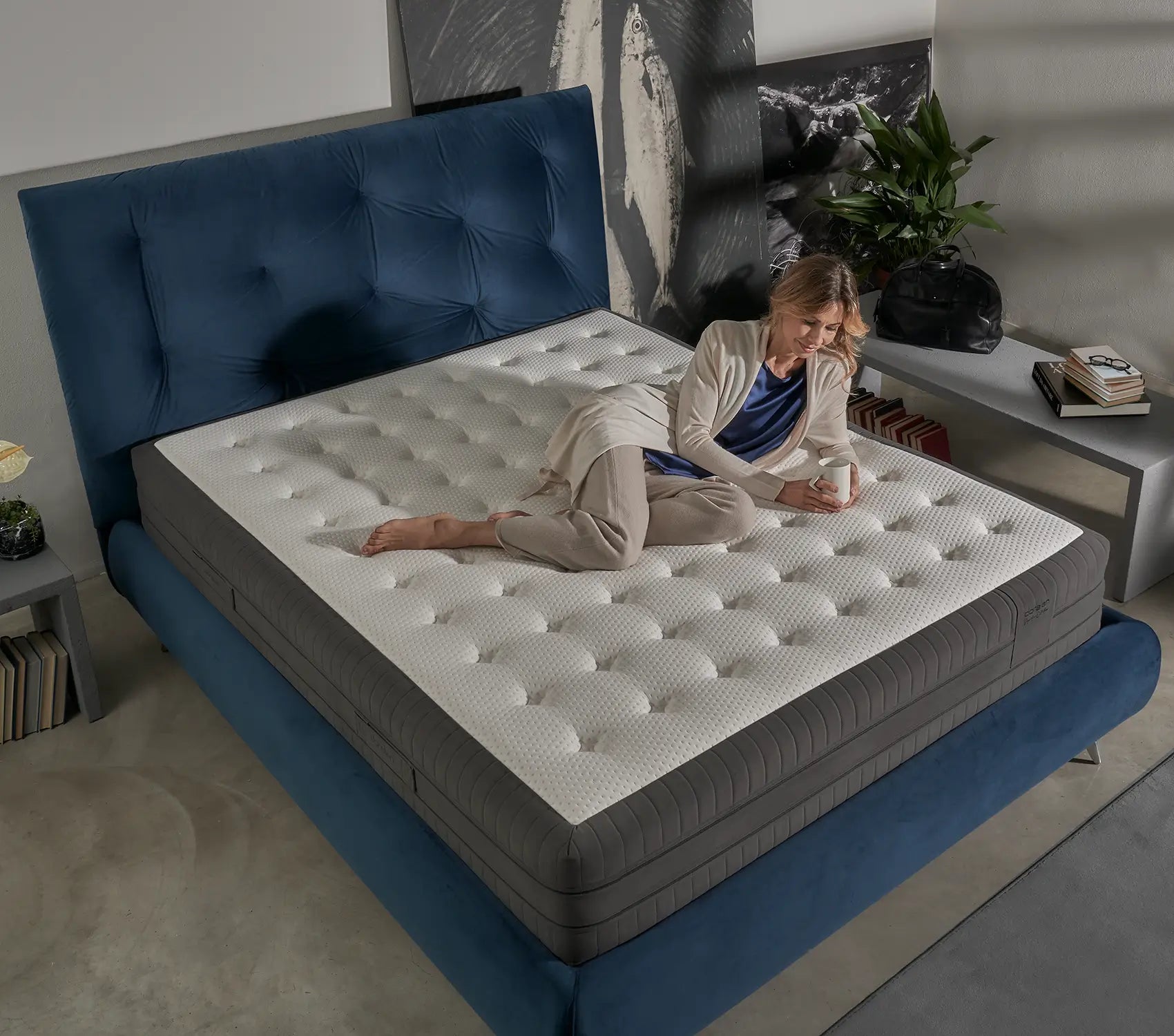 Modern bedroom with a blue upholstered bed and premium quilted mattress, featuring a relaxed woman enjoying a cozy moment.